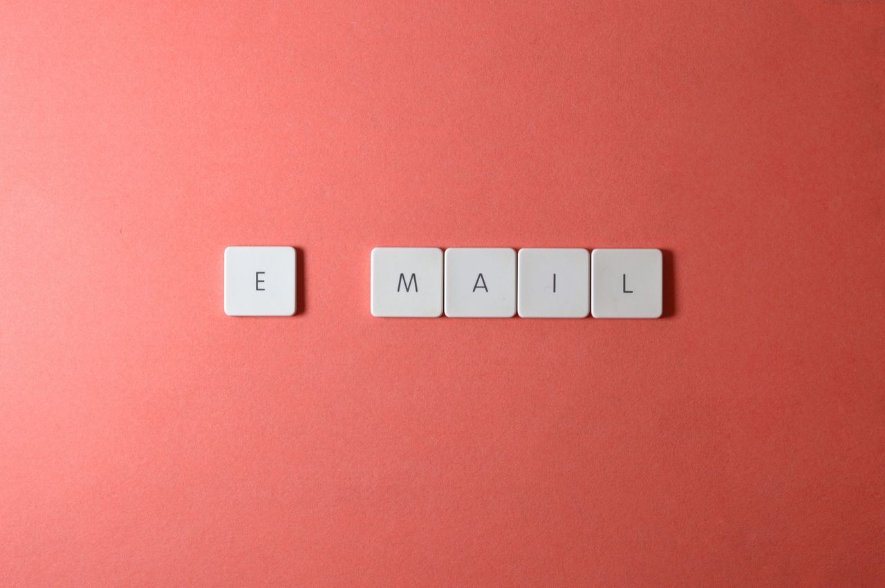 Flat lay of keyboard letter tiles spelling email on coral backdrop.